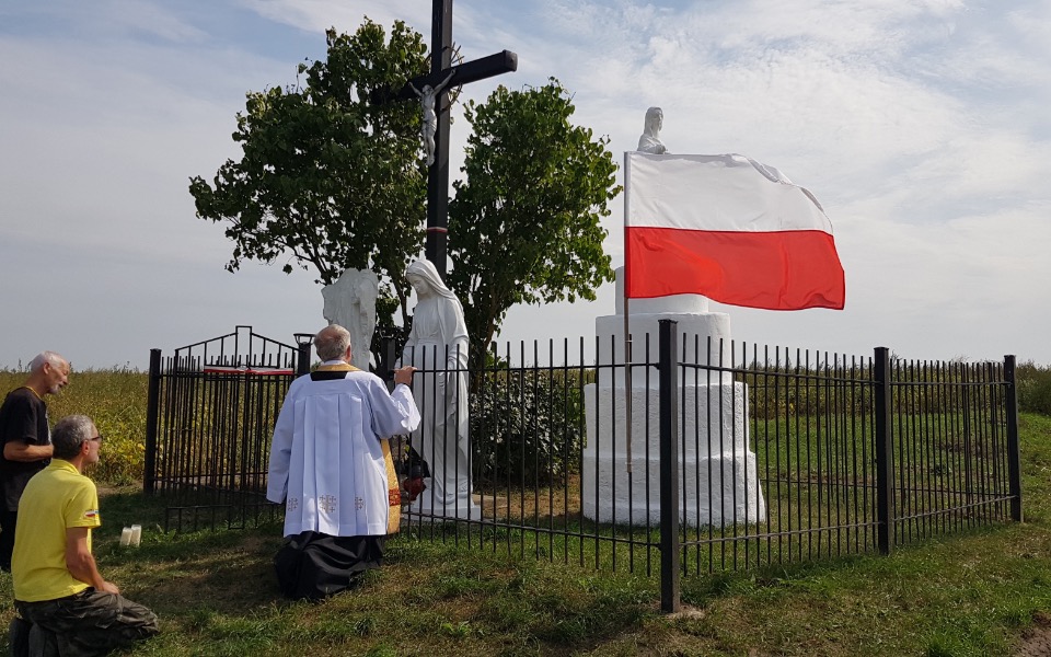 
        Modlitwa przy figurach w otoczeniu polskiej flagi.
    