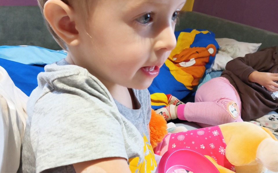 
        Małe dziecko bawi się zabawkami na łóżku.
    