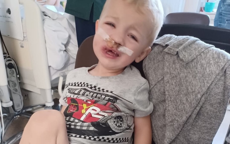 
        Chłopiec z opatrunkiem na twarzy, siedzący w szpitalu.
    