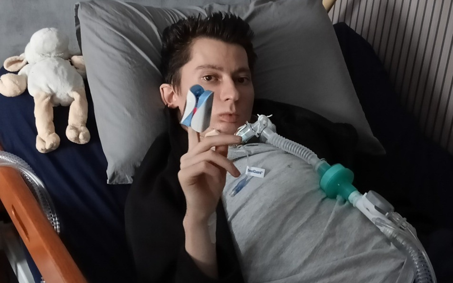 
        Młody mężczyzna leżący w łóżku z urządzeniem medycznym.
    