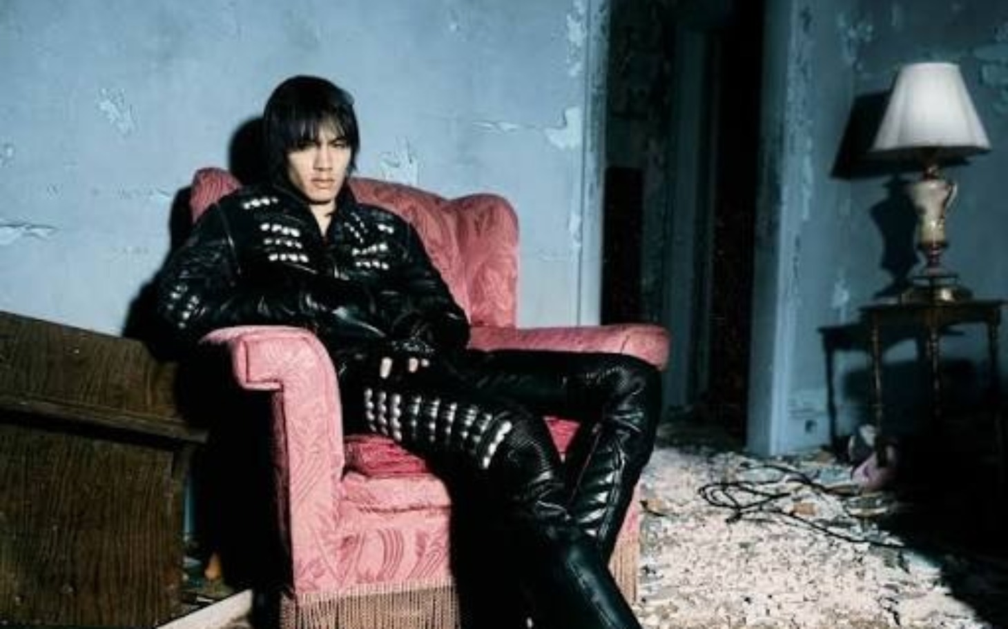 
        Mężczyzna w skórzanej odzieży, siedzący na zniszczonym fotelu.
    