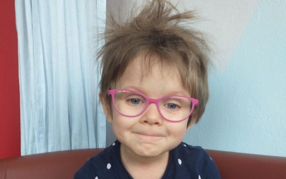 
        Dziecko z okularami i nieładną fryzurą, siedzące na kanapie.
    