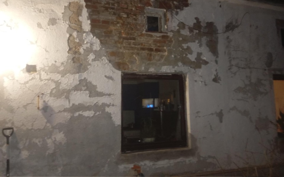 
        Zniszczona ściana budynku z widocznymi śladami uszkodzeń.
    