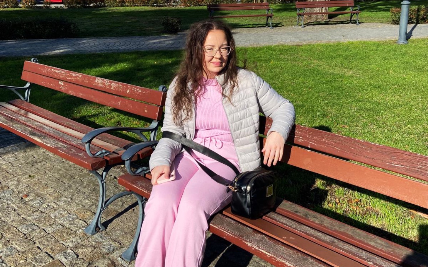 
        Kobieta w okularach siedząca na ławce w parku.
    