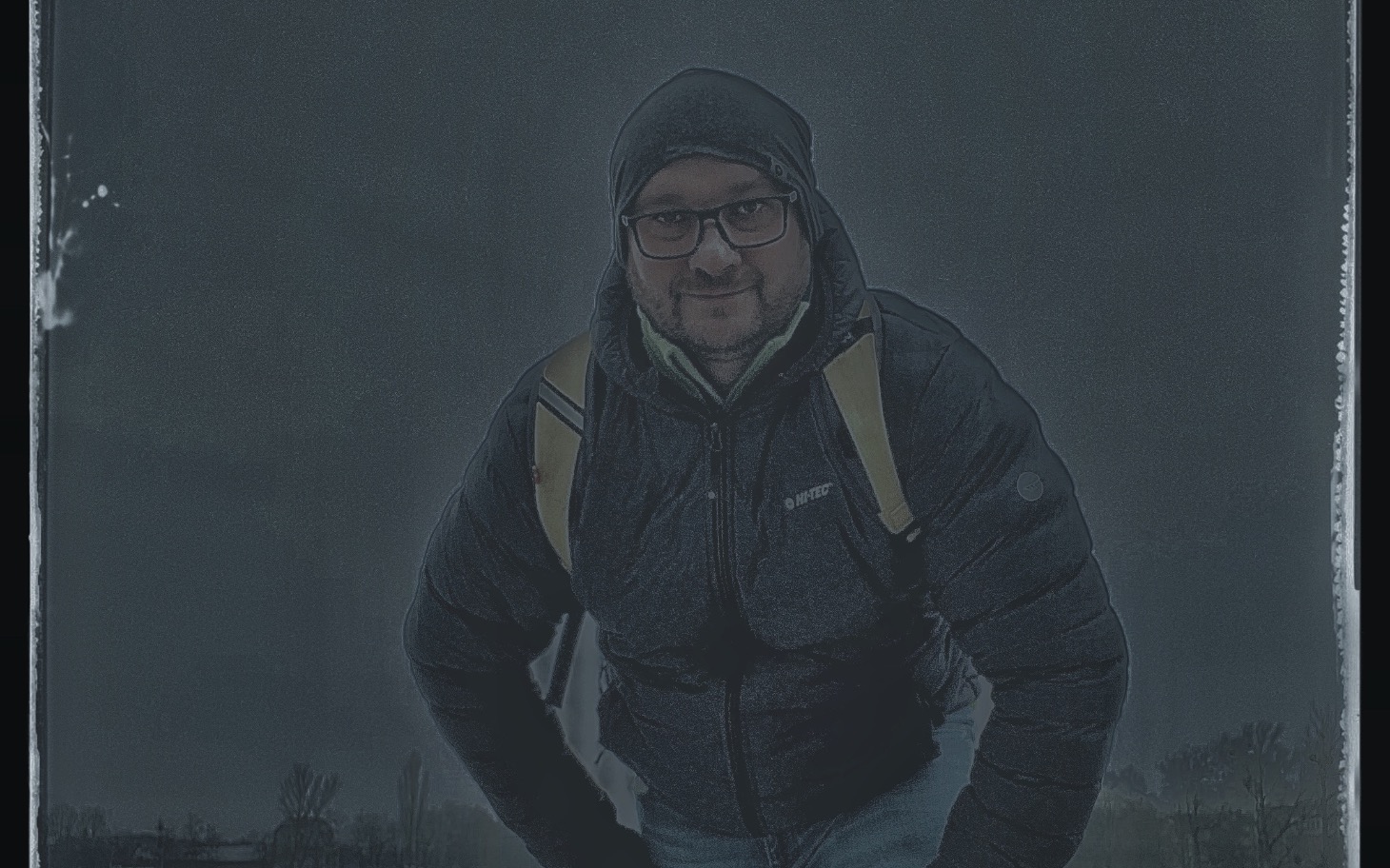 
        Mężczyzna w ciemnej kurtce, pozujący w deszczowej scenerii.
    