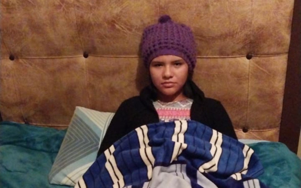 
        Dziewczynka w czapce, siedząca na łóżku z przykryciem.
    