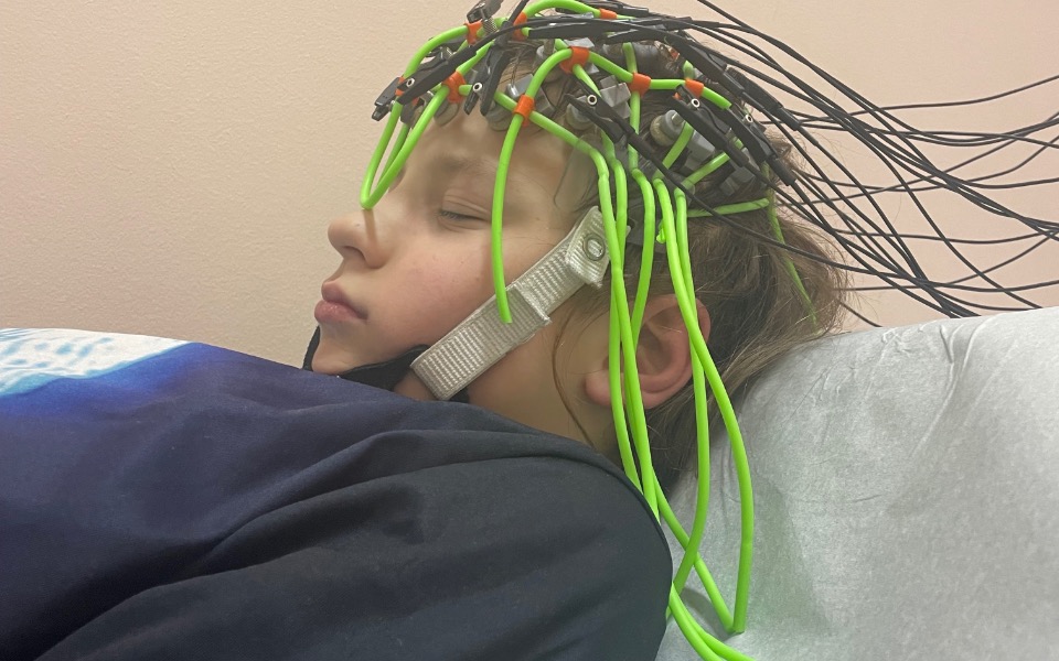 
        Dziecko w trakcie badania EEG, z elektrodami na głowie.
    
