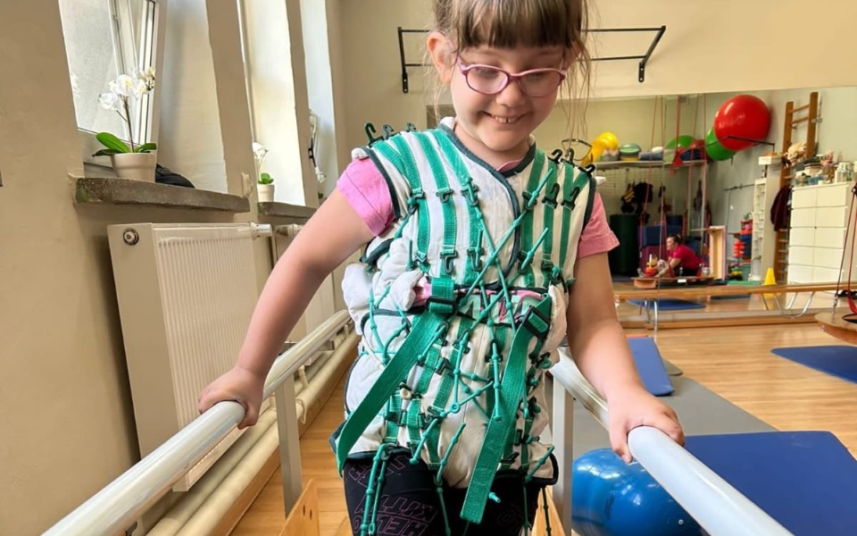 
        Dziewczynka w specjalnej kamizelce, ćwicząca na rehabilitacji.
    