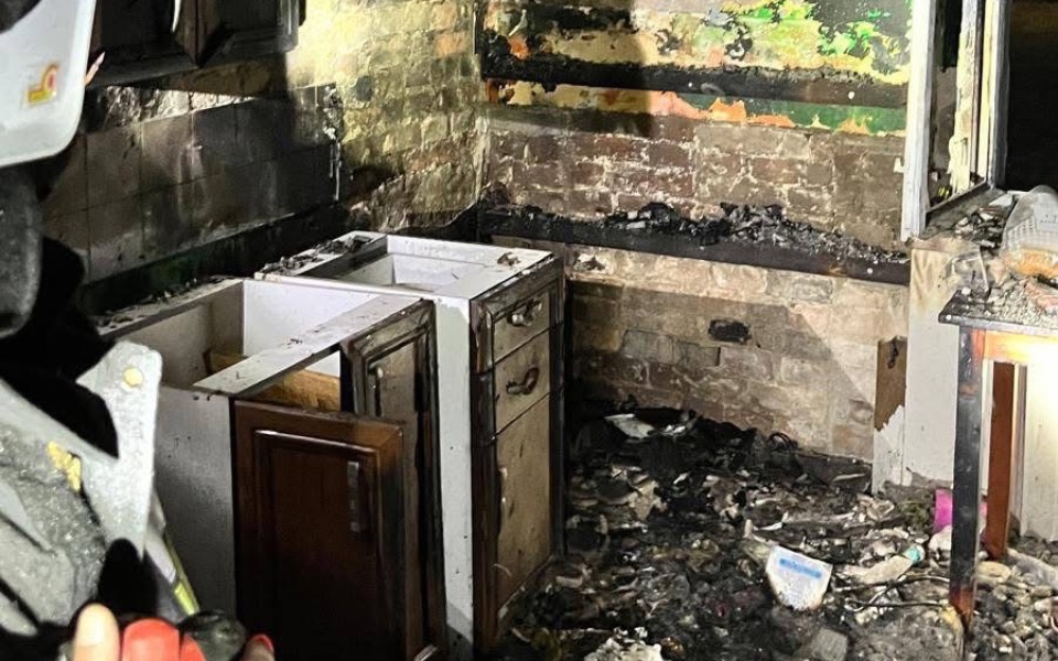 
        Zniszczona kuchnia po pożarze, z popiołem i zniszczonymi meblami.
    