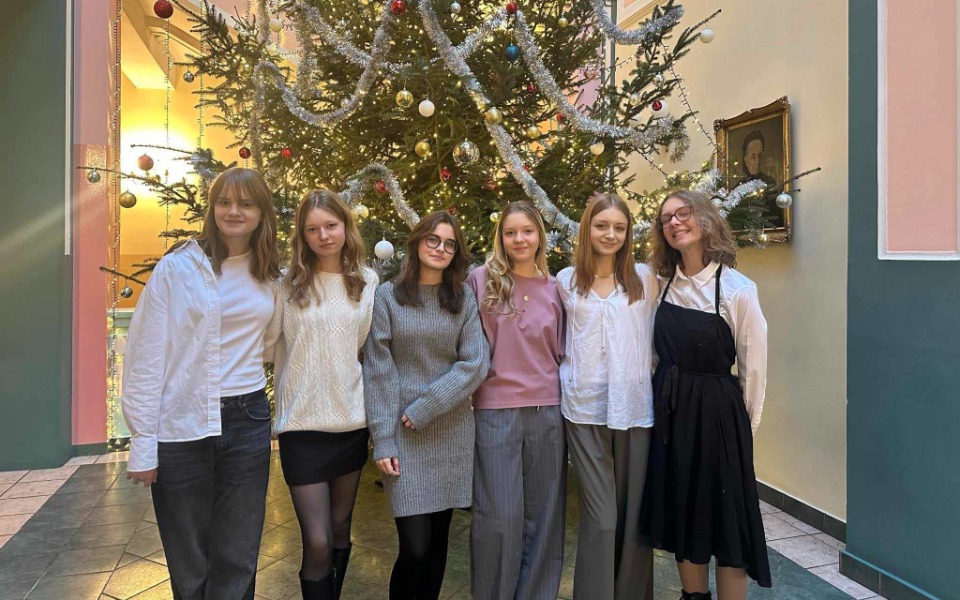 
        Grupa młodych kobiet pozująca przy choince w świątecznym otoczeniu.
    