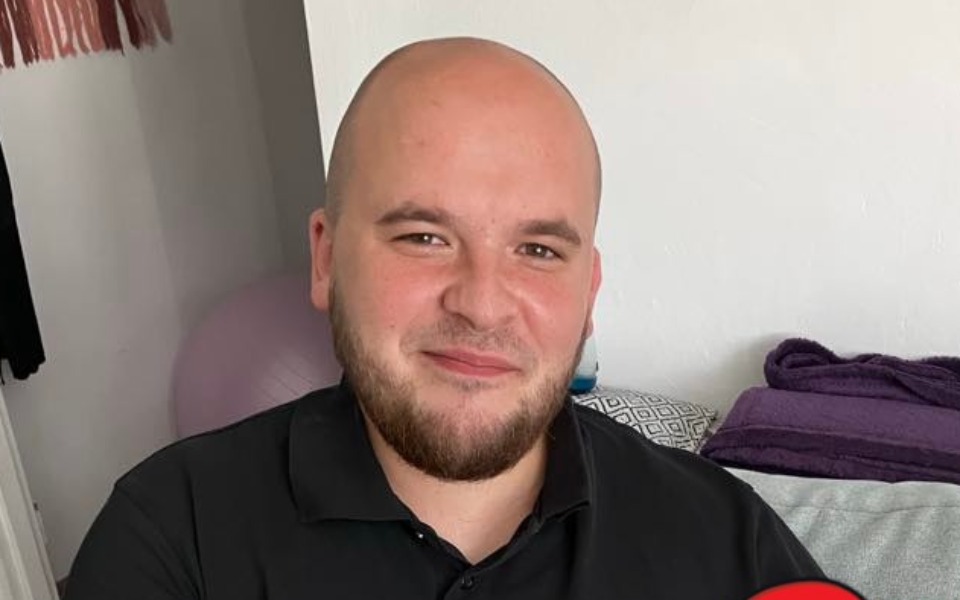 
        Mężczyzna uśmiechający się do kamery w domowym otoczeniu.
    