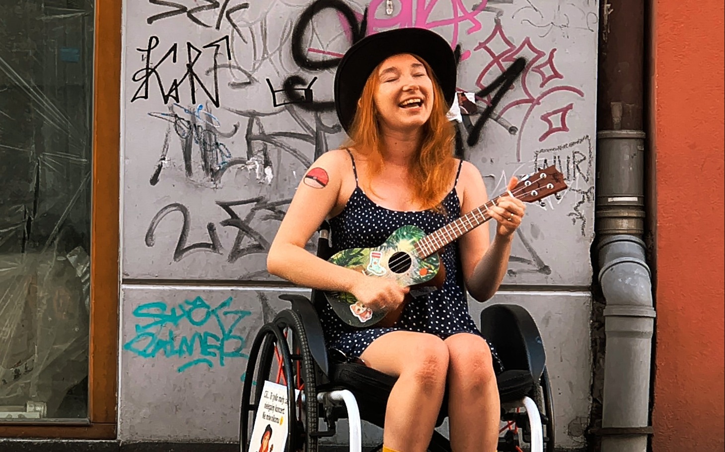 
        Kobieta grająca na ukulele w wózku inwalidzkim.
    