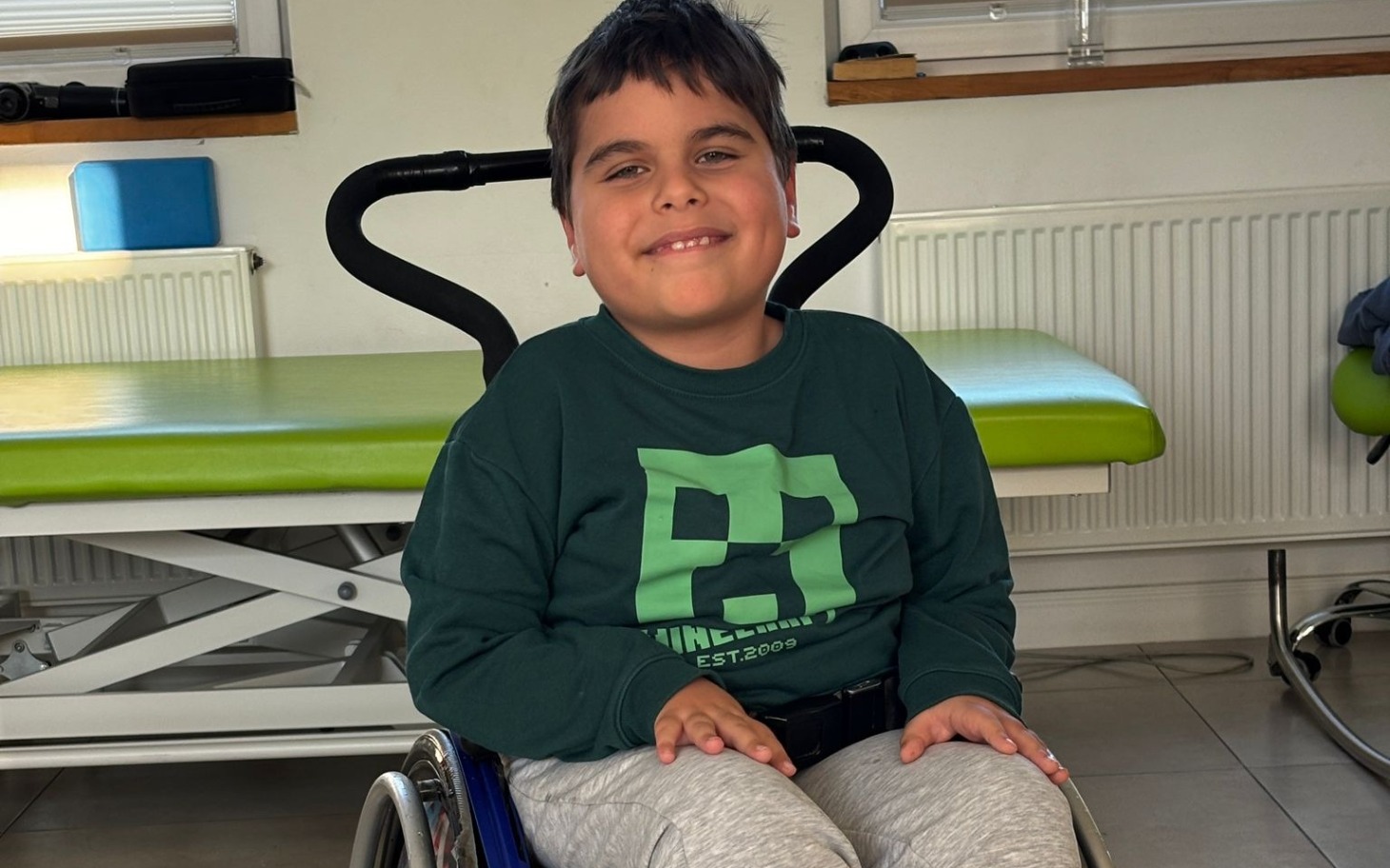 
        Chłopiec na wózku inwalidzkim uśmiechający się do kamery.
    