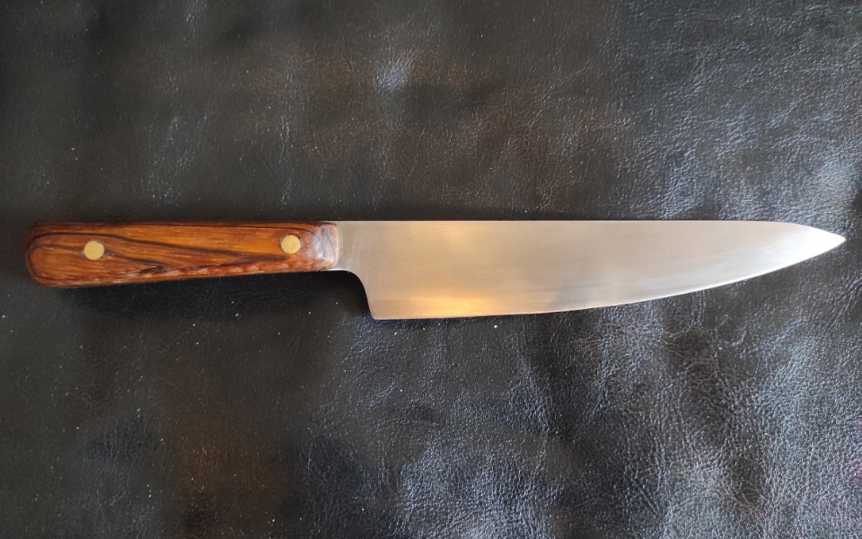 
        Ostry nóż kuchenny z drewnianą rączką na czarnym tle.
    