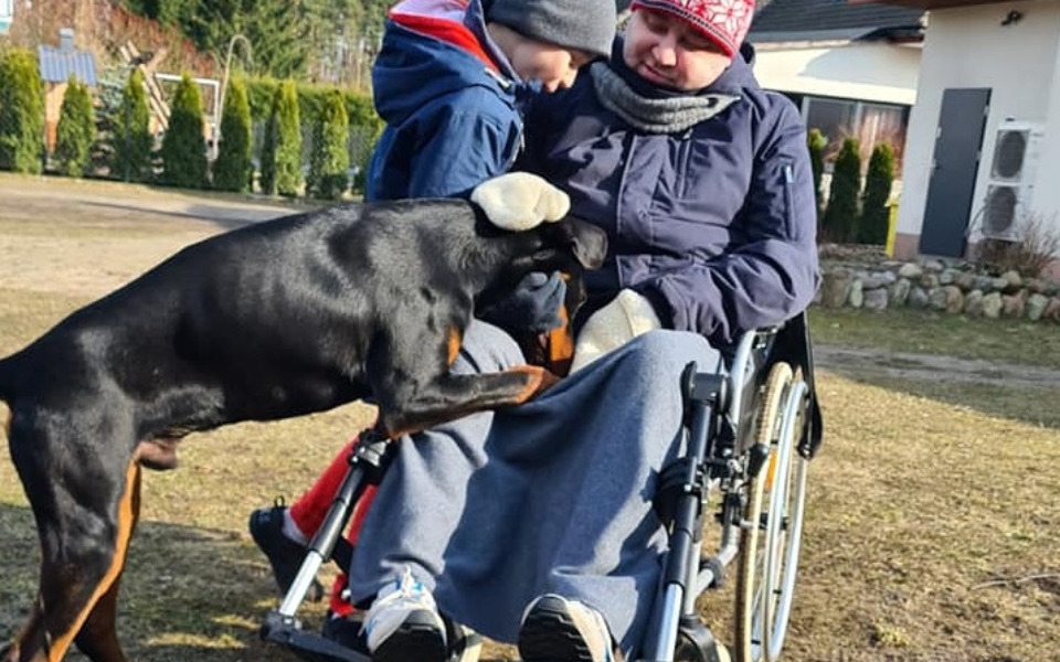 
        Kobieta na wózku inwalidzkim z dzieckiem i psem.
    