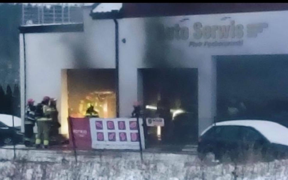 
        Pożar w warsztacie, strażacy gaszą ogień w zimowej scenerii.
    