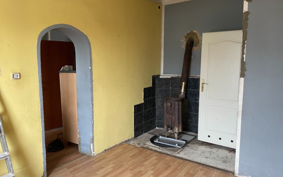 
        Pusty pokój z żółtymi ścianami i piecem, gotowy do remontu.
    