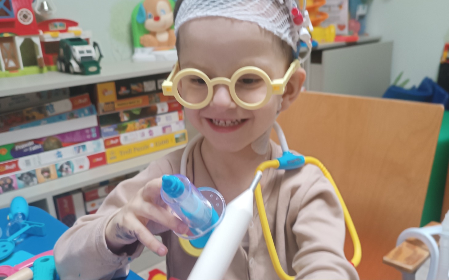 
        Uśmiechnięty chłopiec w okularach, bawiący się w szpitalu.
    