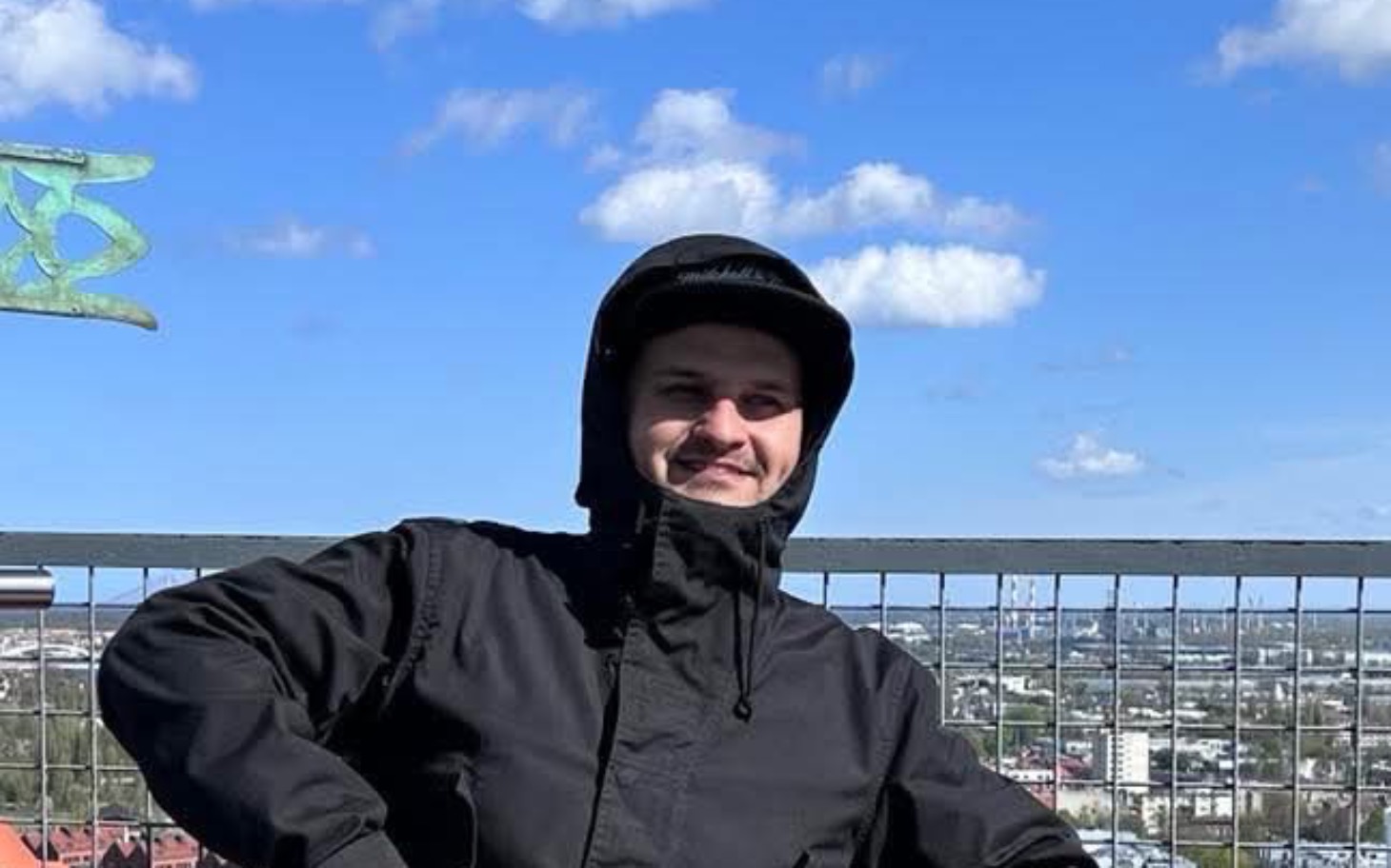
        Mężczyzna w kasku na tle miasta, uśmiechający się do kamery.
    