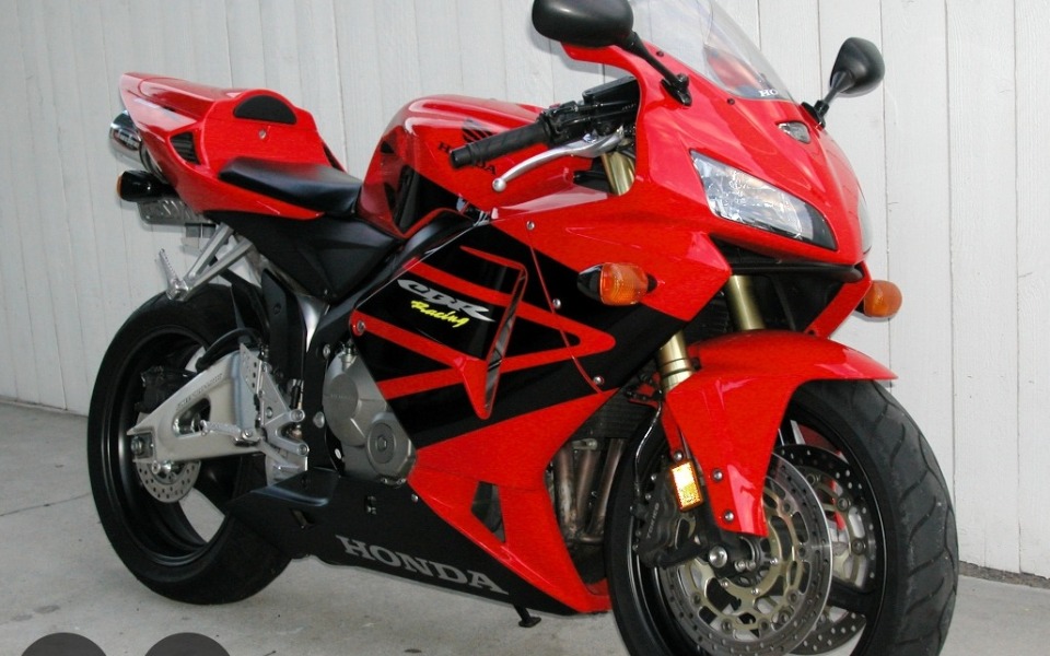 
        Czerwony motocykl Honda, zaparkowany na tle białej ściany.
    