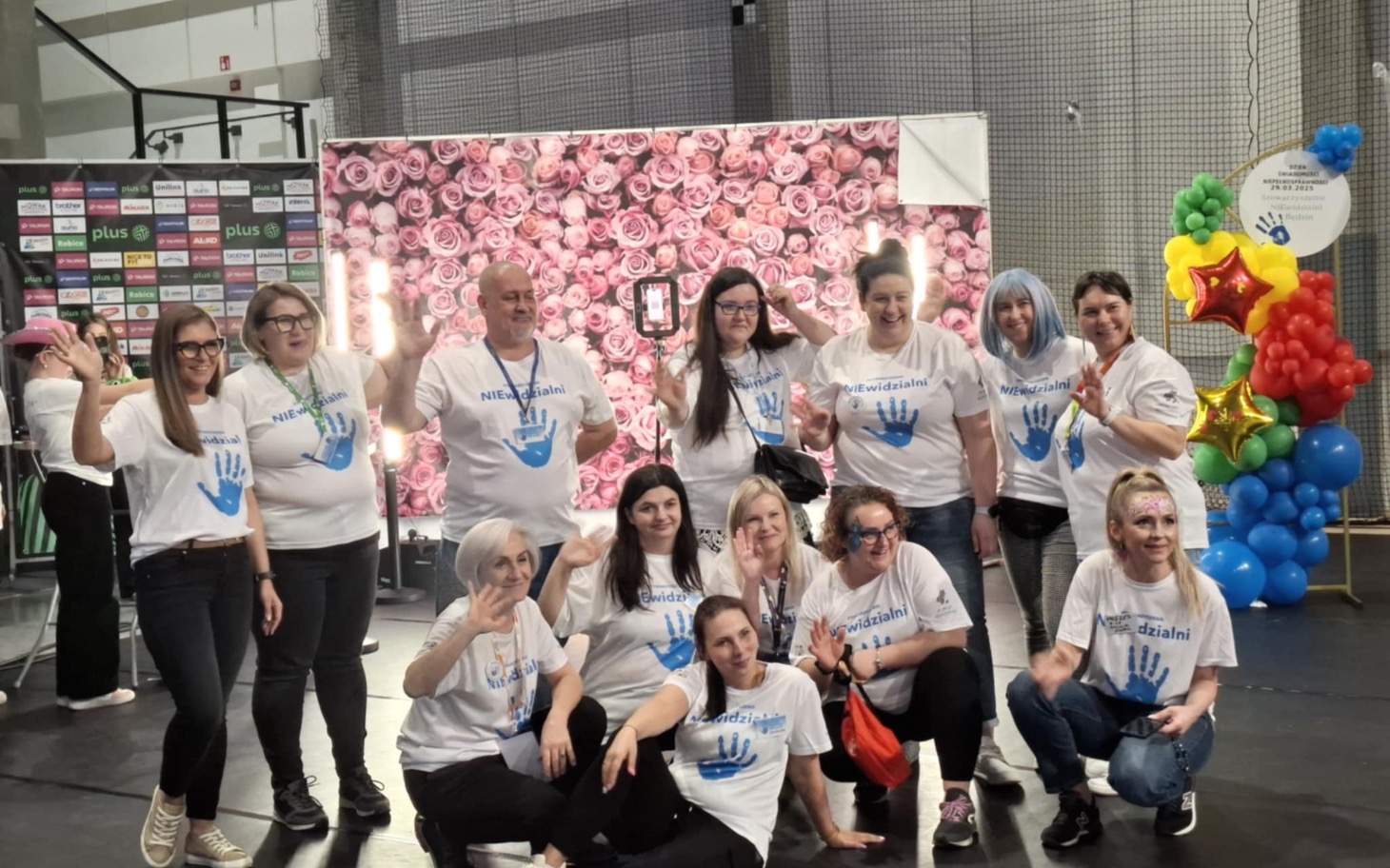 
        Grupa ludzi w białych koszulkach z niebieskimi odciskami dłoni.
    