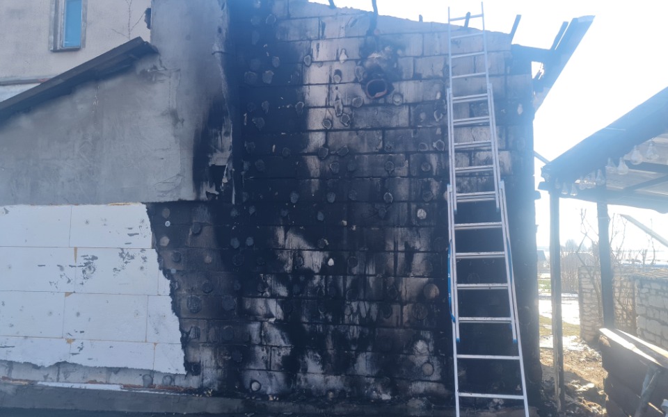 
        Zniszczona ściana budynku po pożarze, widoczna drabina.
    