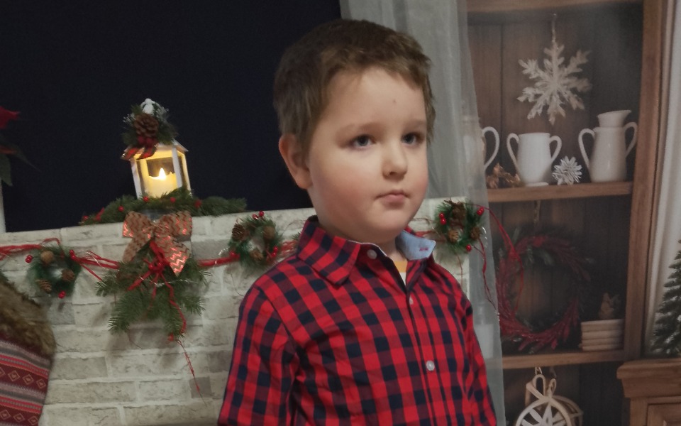 
        Chłopiec w czerwonej koszuli na tle dekoracji świątecznych.
    