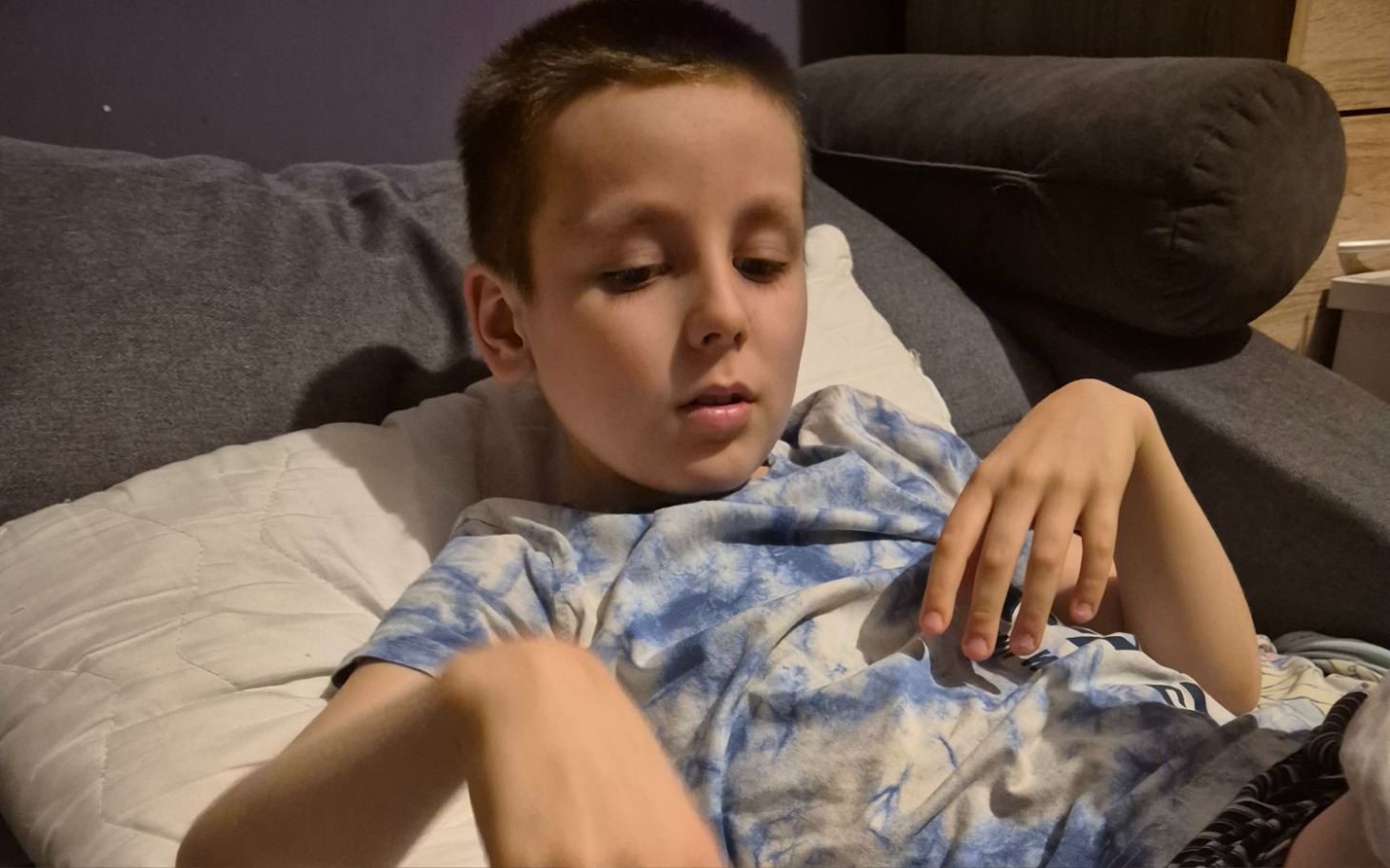 
        Chłopiec leżący na kanapie, skupiony na czymś.
    