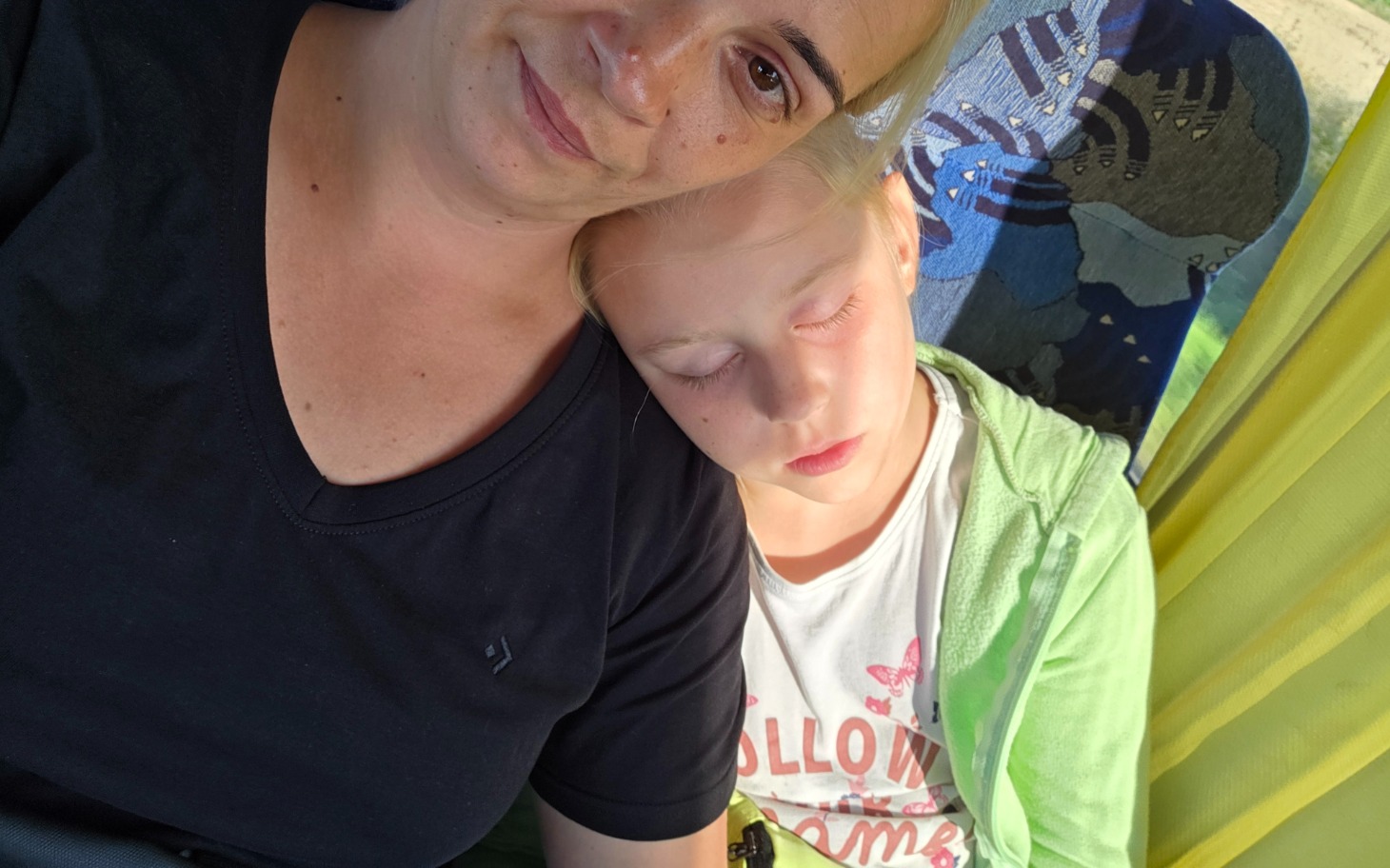 
        Mama z dzieckiem śpiącym na jej ramieniu w parku.
    