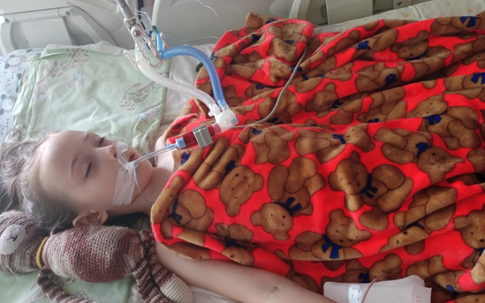 
        Dziewczynka leżąca w szpitalu, z maską tlenową i kocem.
    