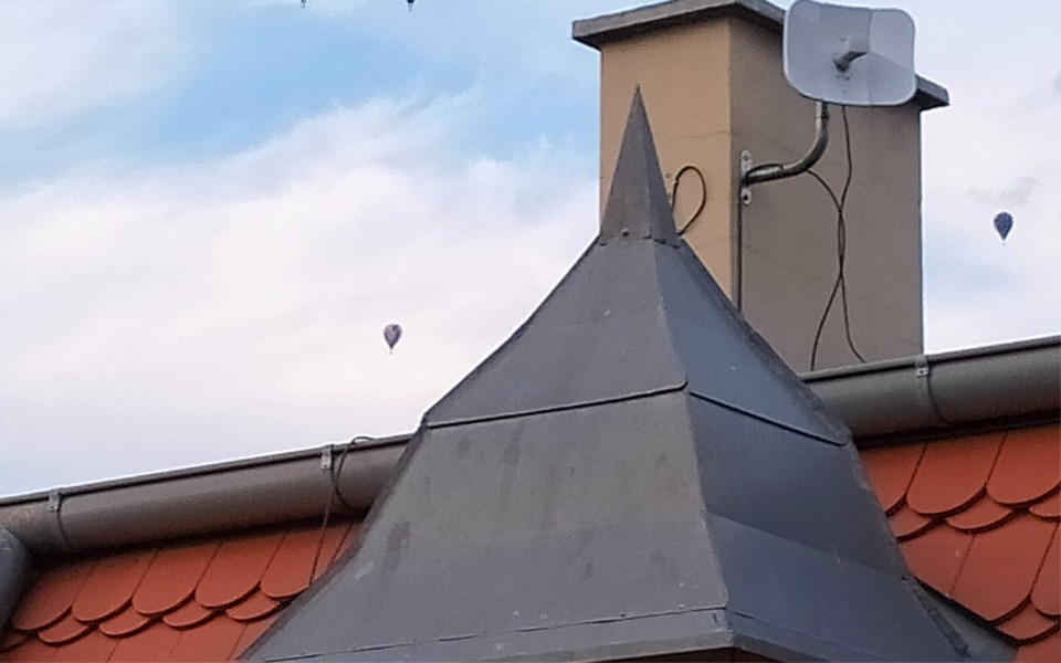 
        Widok dachu z kominem i balonami na niebie w tle.
    