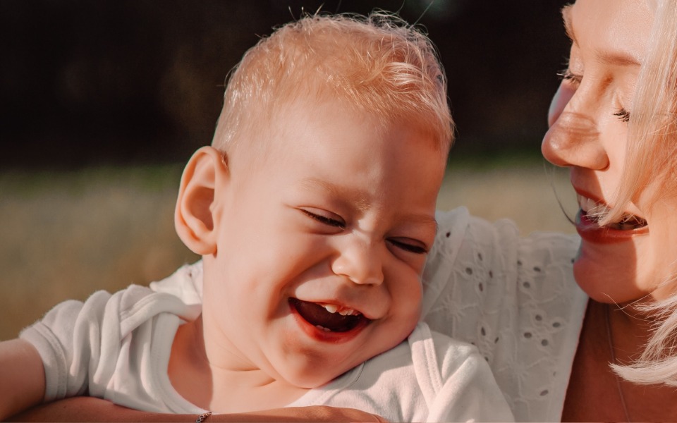 
        Szczęśliwe dziecko w ramionach matki, uśmiechające się radośnie.
    