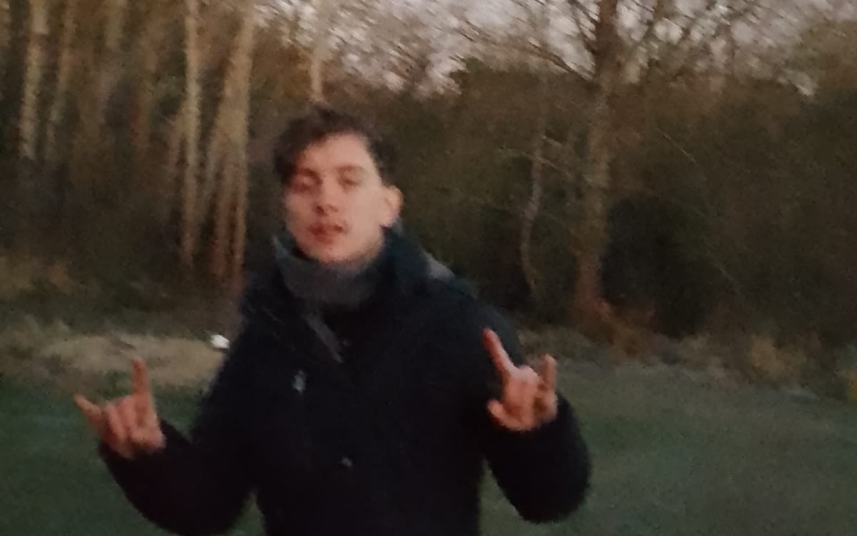 
        Młody mężczyzna w ciemnym płaszczu, pokazujący znak pokoju.
    