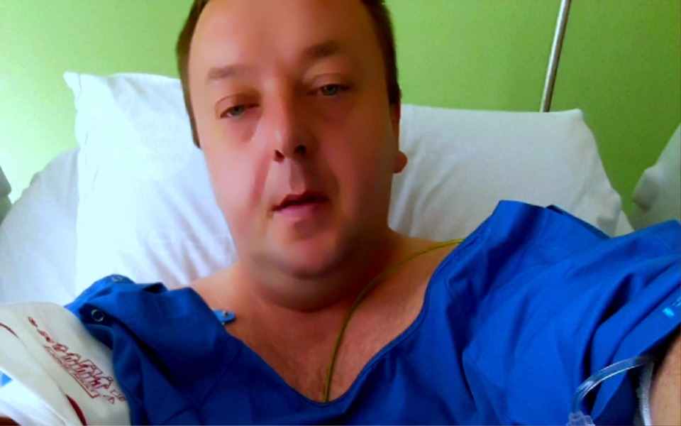 
        Mężczyzna w szpitalu, w niebieskim fartuchu, z kroplówką.
    