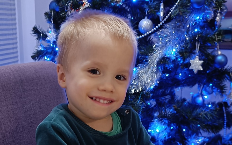 
        Uśmiechnięty chłopiec siedzący przy choince.
    