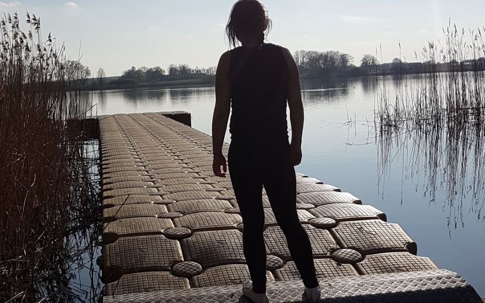 
        Postać na pomoście, z widokiem na spokojne jezioro.
    