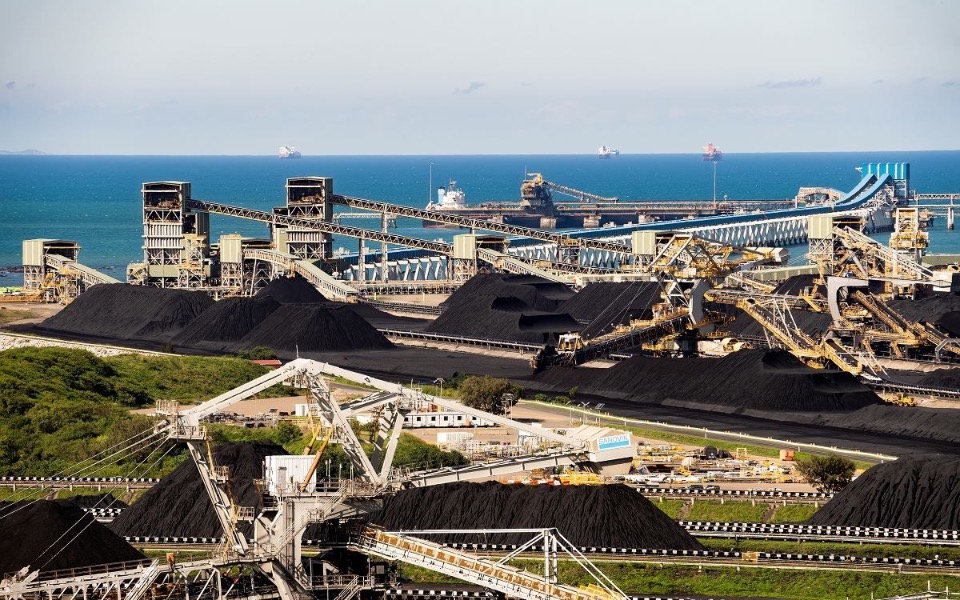 
        Widok na przemysłowy port z węglem i statkami na tle morza.
    