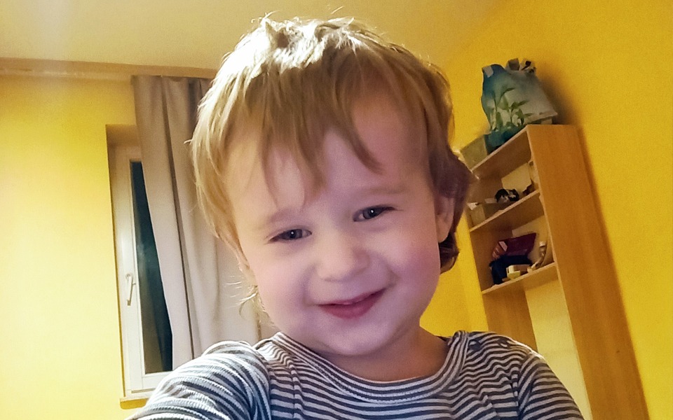 
        Mały chłopiec uśmiecha się do kamery w kolorowym pokoju.
    