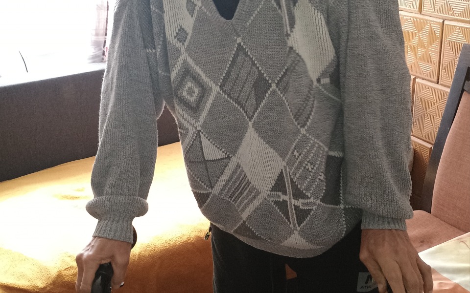 
        Osoba starsza z laską, w swetrze w romby.
    