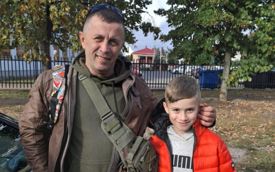 
        Mężczyzna z dzieckiem na tle parku.
    