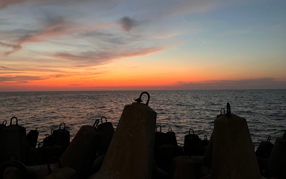 
        Zachód słońca nad morzem, z widokiem na betonowe elementy.
    