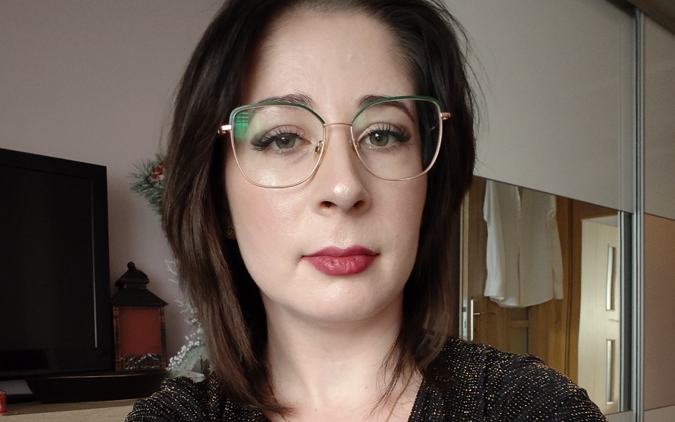 
        Kobieta w okularach, patrzy w obiektyw z uśmiechem.
    