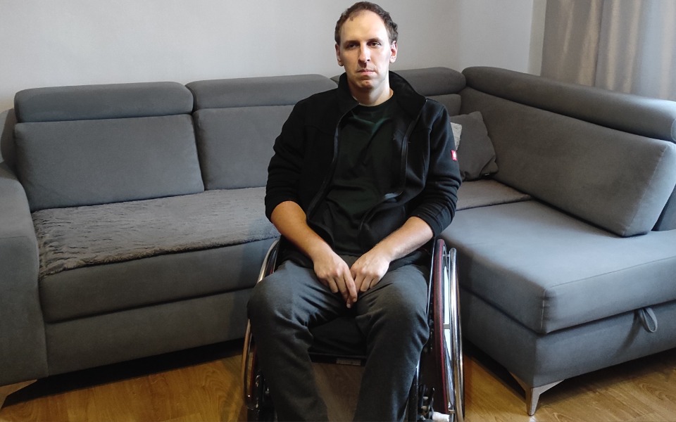 
        Mężczyzna na wózku inwalidzkim, siedzący na kanapie w salonie.
    