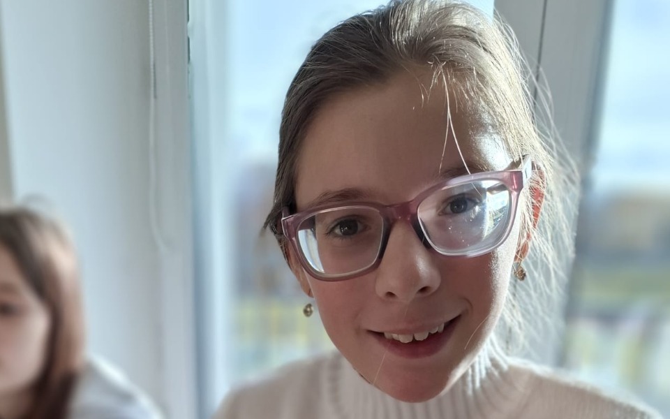 
        Uśmiechnięta dziewczynka w okularach, w jasnym otoczeniu.
    