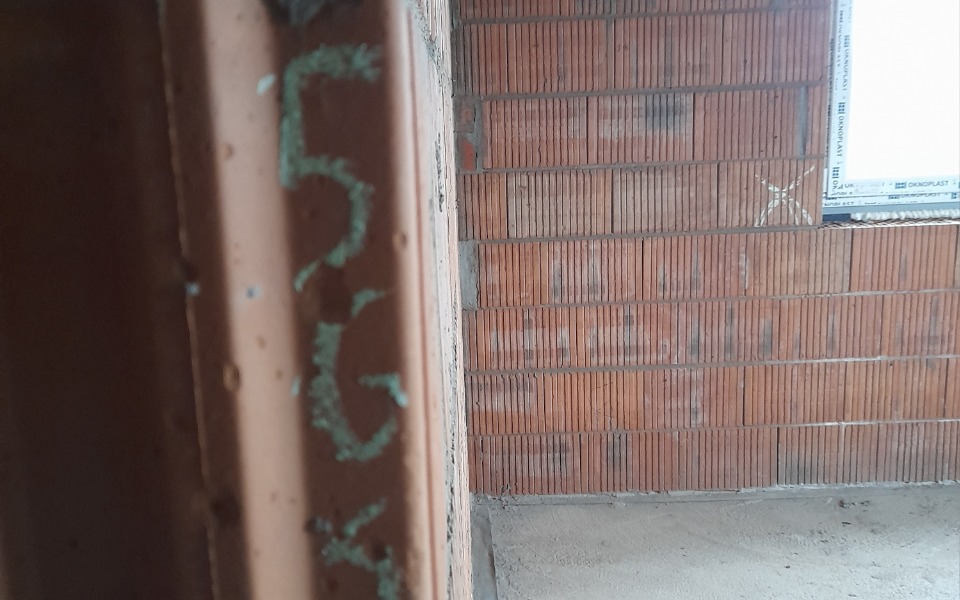 
        Fragment ściany z cegłami, z widocznymi numerami na tynku.
    