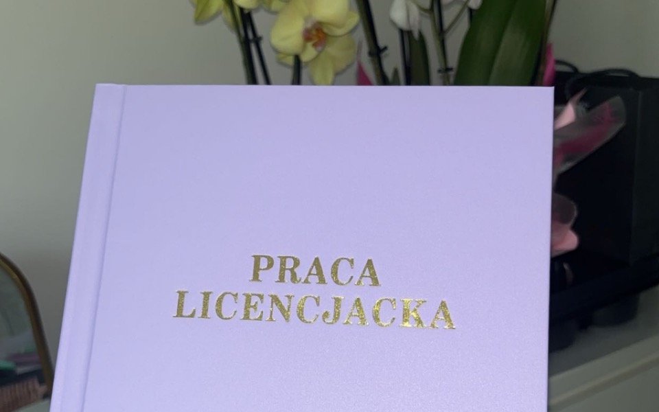 
        Osoba trzymająca różową pracę licencjacką z napisem 'PRACA LICENCJACKA'.
    