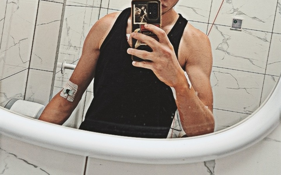 
        Młody mężczyzna w lustrze, pokazuje opatrunek na ramieniu.
    