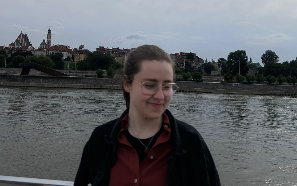 
        Osoba na tle rzeki i miasta, uśmiechnięta.
    