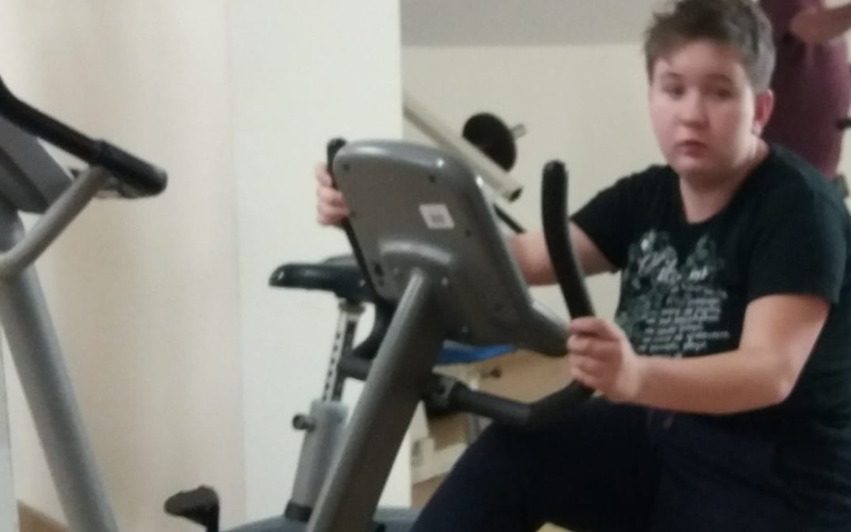 
        Młoda osoba na rowerze stacjonarnym w siłowni.
    