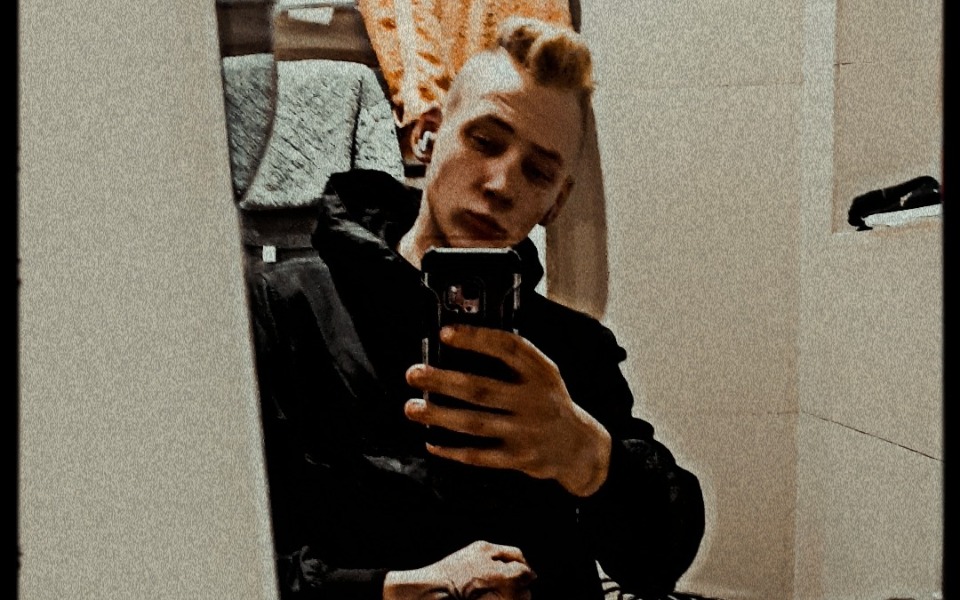 
        Młody mężczyzna robi selfie w lustrze w ciemnym ubraniu.
    